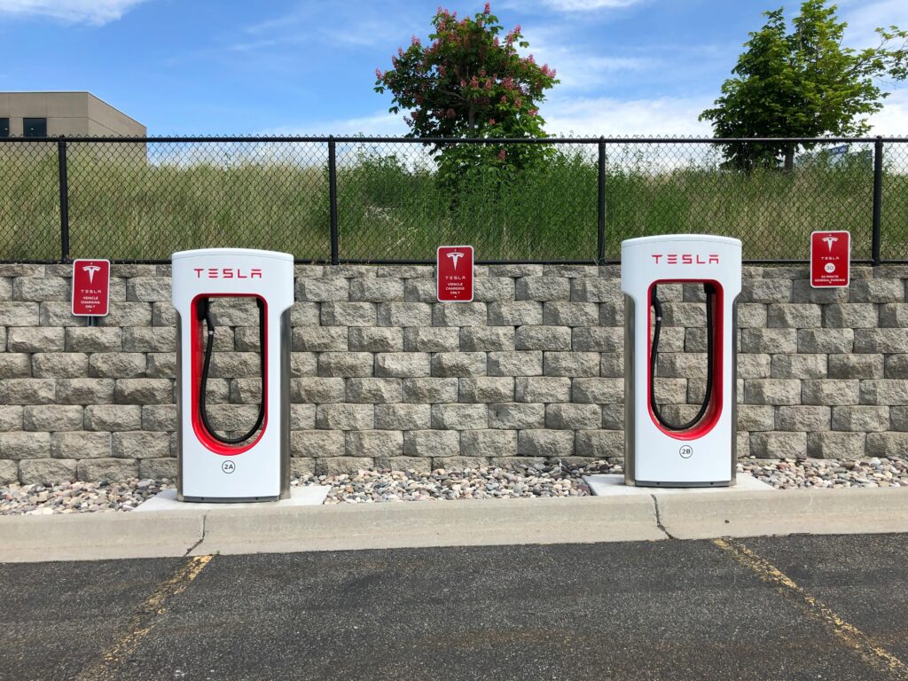 Cuánto cuesta cargar un coche eléctrico cada 100 km en España (2026) Dual Tesla electric car chargers in Idaho Falls parking lot with clear blue sky.